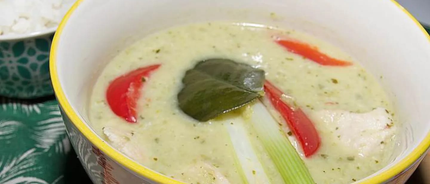 A traditional bowl of creamy, aromatic Thai green curry with chunks of chicken in a small bowl with jasmine rice