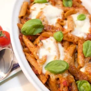Cheesy pasta dish with vegetarian sausages and topped with mozzarella cheese and basil