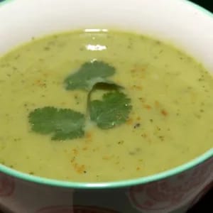 Watercress soup with a sprig of coriander as garnish in a white bowl with green trim